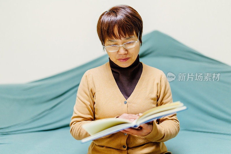 一位戴着老花镜的中年妇女坐在沙发上看书，这是一种简单的生活方式
