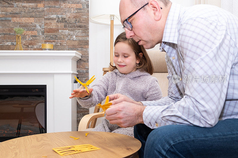 一个白种人家庭，一个男人和一个女孩，一个7岁的孩子，用胶合板组装了一只木制蜻蜓。