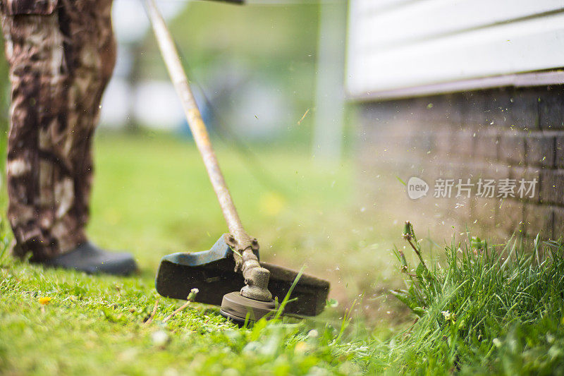 男子在后院用电动或汽油草坪修剪机修剪高草。园艺护理工具和设备。用手动割草机修剪草坪的过程
