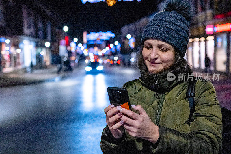 晚上在外面玩手机的年轻快乐的女人。