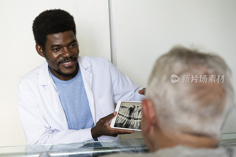 非裔美国男性牙医在她的办公室里通过电子平板电脑向老年病人展示全景颌x光
