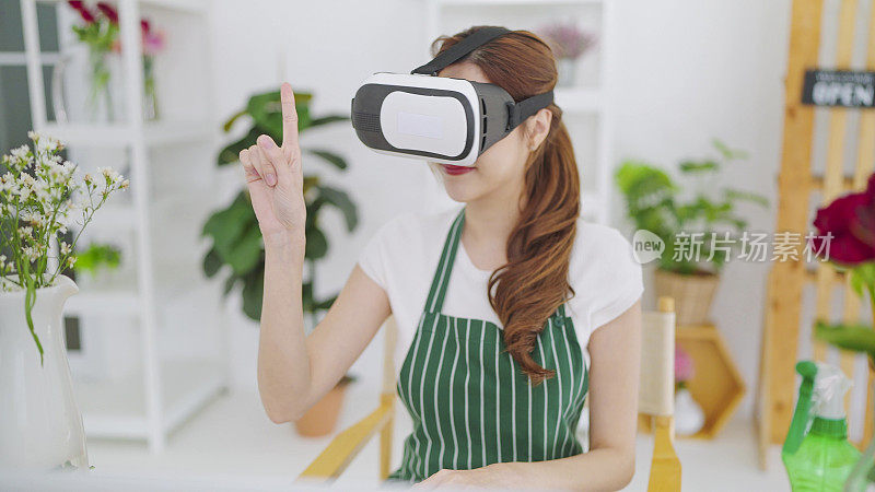 年轻的亚洲女性戴着VR眼镜开花店，在空中挥动双手，通过虚拟现实耳机挑选鲜花。商业和技术理念，虚拟虚拟