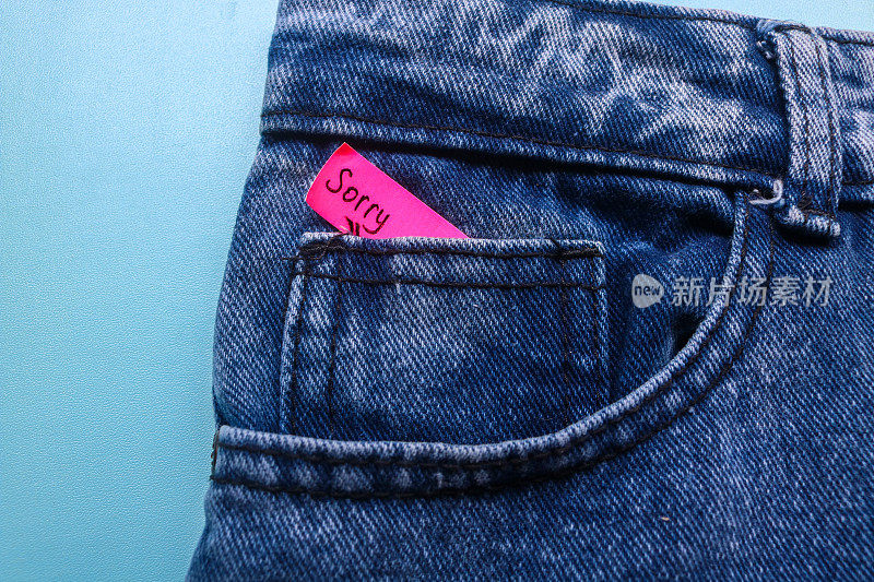 “对不起”这个词写在牛仔裤口袋里一张蓝色背景的红色便利贴上。道歉的概念