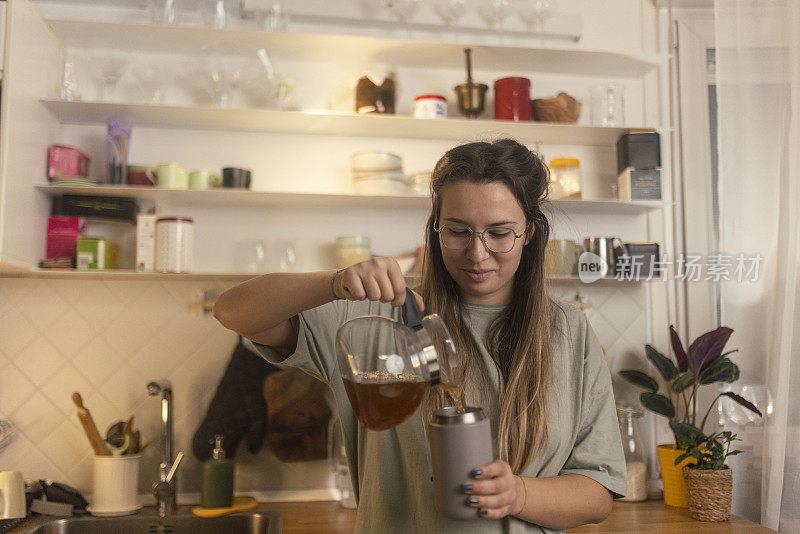 一个面带微笑的女人把茶壶里的茶倒进可重复使用的灰色杯子里