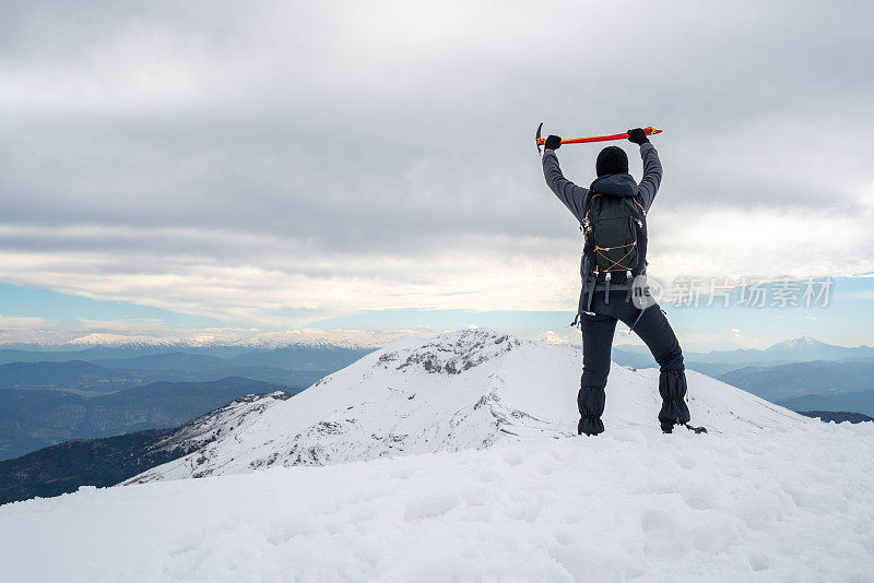 图为，一名女登山者站在高海拔的山顶上，手持冰镐望着群山。