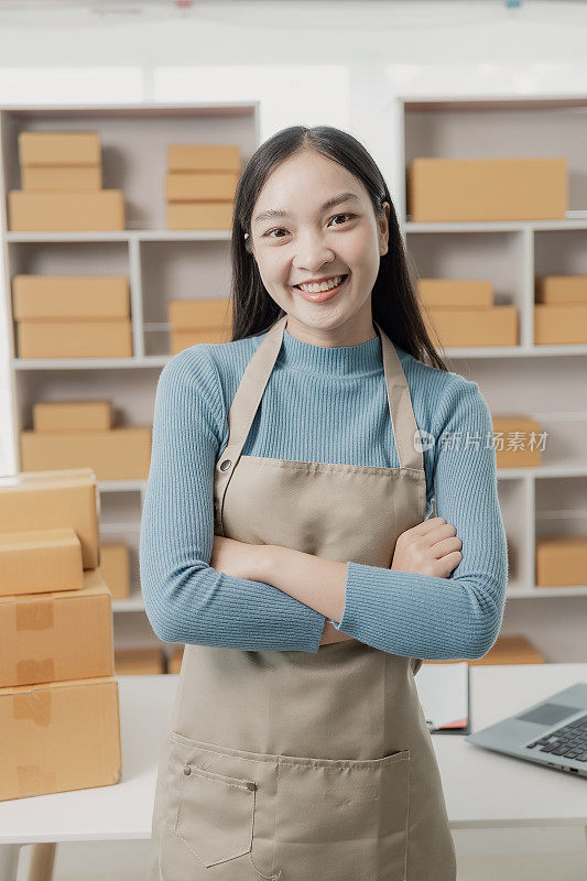 邮包，网上销售概念中小企业创业。一个穿着围裙的独立亚洲女性的小企业主用笔记本电脑和盒子在网上接受订单。中小企业业务。