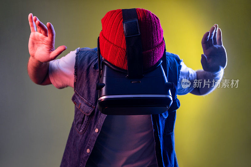 戴着虚拟现实头盔的玩家站着，举起手臂，向下看，玩游戏或飞行。