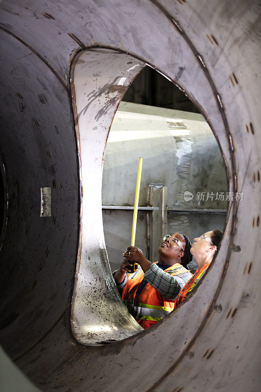 两个妇女在金属制造车间测量物体