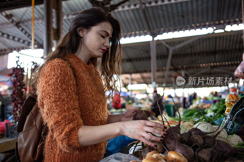 一名年轻女子在当地食品市场购买新鲜水果和蔬菜的照片