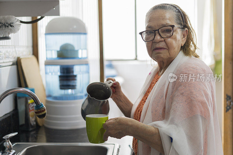 老奶奶站在自己的房子里，看着拍摄她的镜头