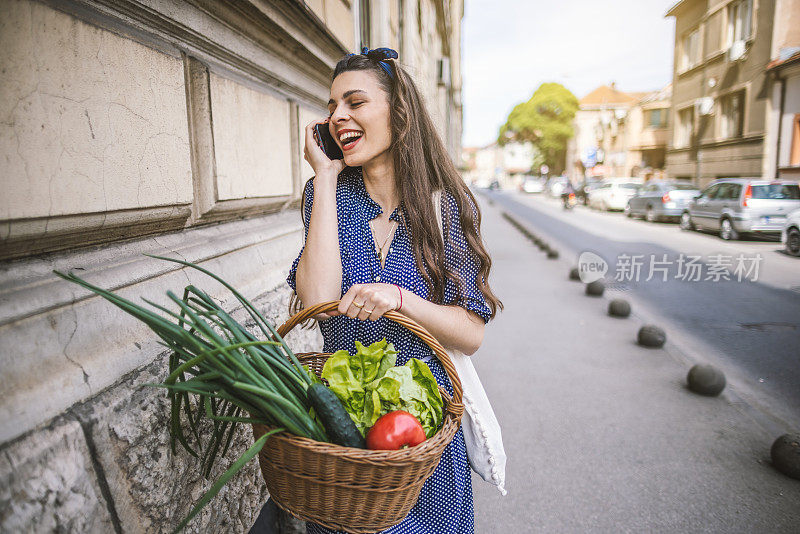 女人用手机，拎着装满食品杂货的购物篮