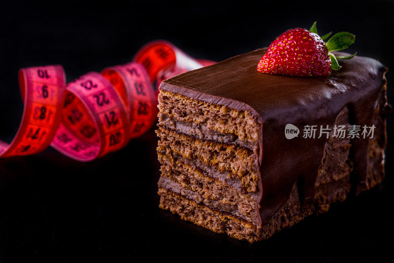 蜂蜜蛋糕覆盖巧克力釉草莓和卷尺在黑色背景。水平方向