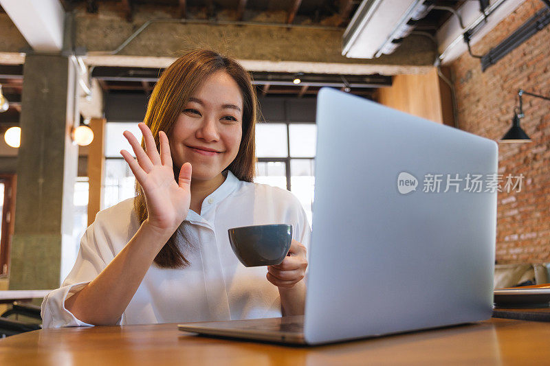 一位漂亮的年轻女子在咖啡馆喝咖啡时，用笔记本电脑进行视频通话、在线会议