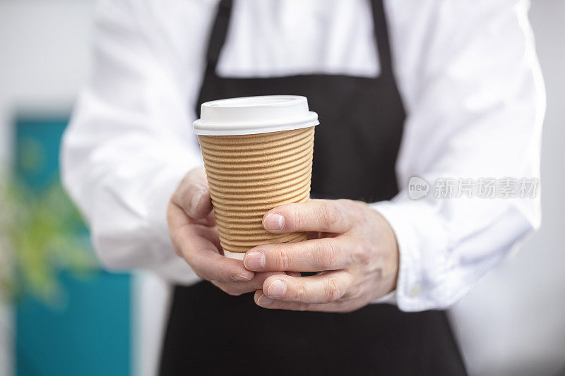 服务员咖啡师拿着一个可取出的一次性纸杯热咖啡在咖啡馆