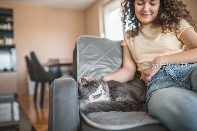 一个年轻的女人和她的猫坐在客厅的沙发上休息