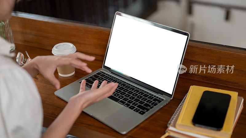 一个女人在咖啡店远程办公，正在开在线会议，桌上放着一个笔记本电脑模型。