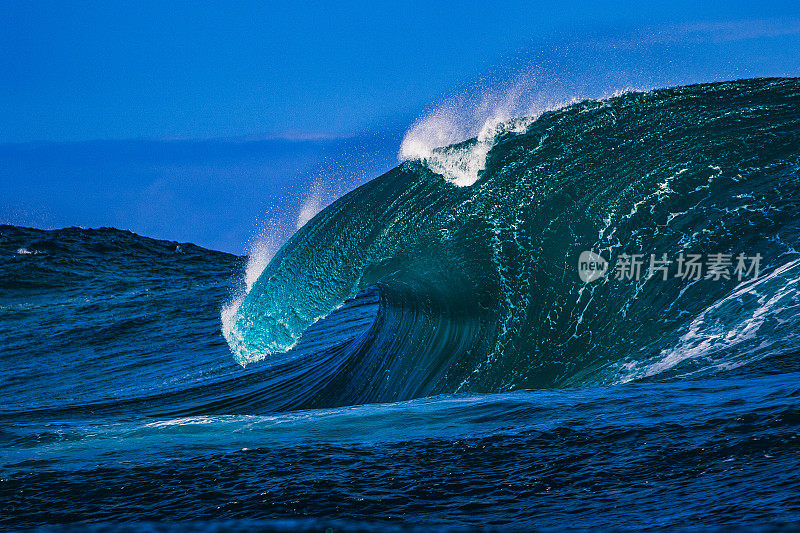 巨大的蓝色弯曲波浪在开阔的海洋上冲破一个浅海礁