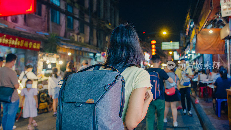 年轻的亚洲女性背包客在泰国曼谷的夜晚走在街上。假日度假旅行。