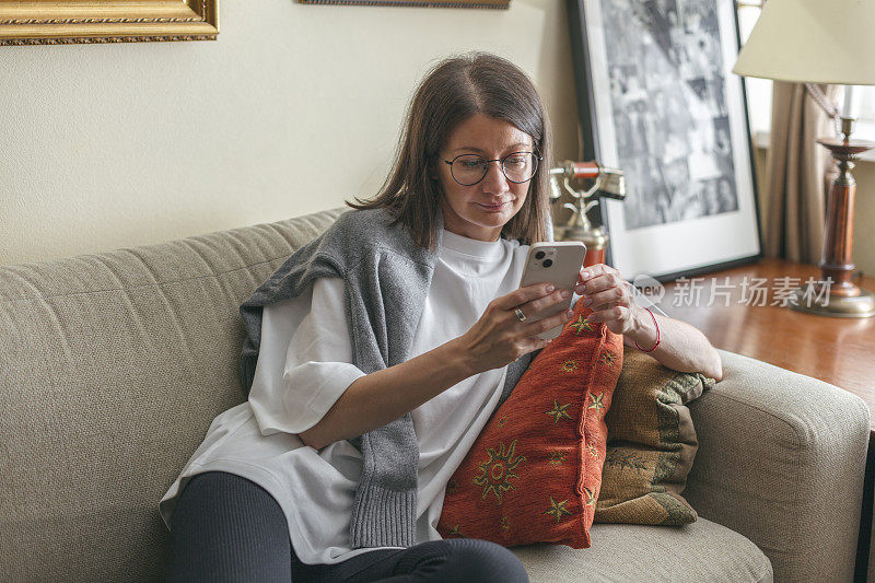 年轻的成年女子坐在客厅的沙发上玩手机