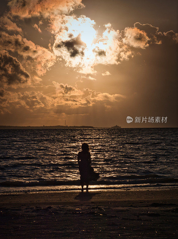日落时，一位妇女望着面朝大海的地平线
