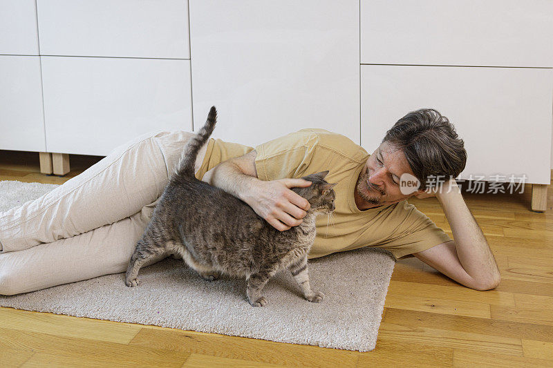 一个男人躺在地板上抚摸他的猫