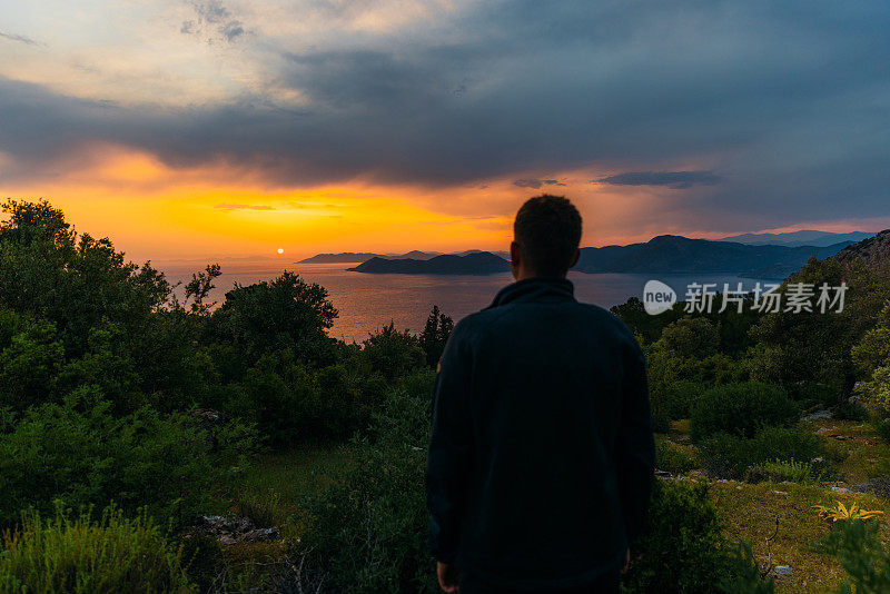 男子欣赏神奇的日落俯瞰大海和山脉