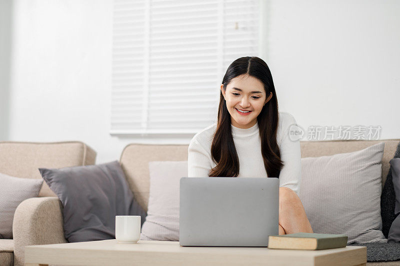在光线充足的客厅里，一名年轻女子舒舒服服地坐在沙发上使用笔记本电脑，看上去很开心。