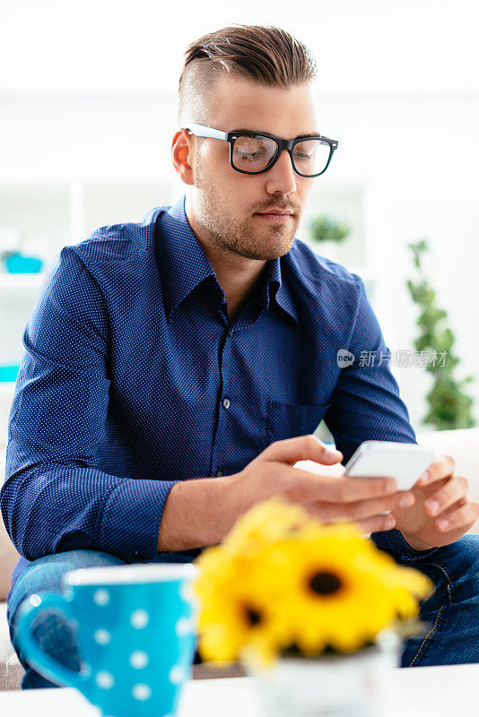 一个留着现代发型的潮人在喝咖啡休息的时候用他的智能手机