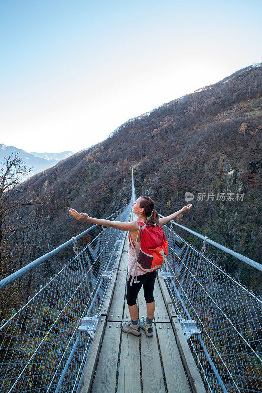 年轻女子在吊桥上徒步旅行，双臂张开