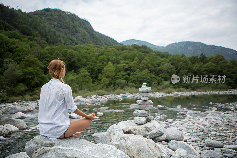 一个女人在河边的岩石上练瑜伽