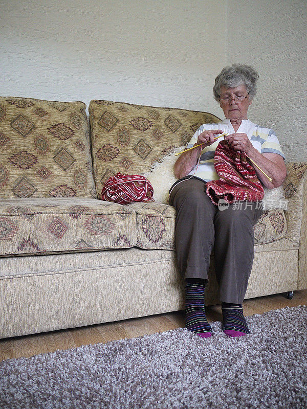 老女人在沙发上休息，织着毛线。
