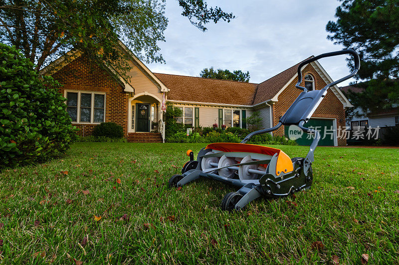 旋转推割草机在绿色草坪上，砖家的背景。