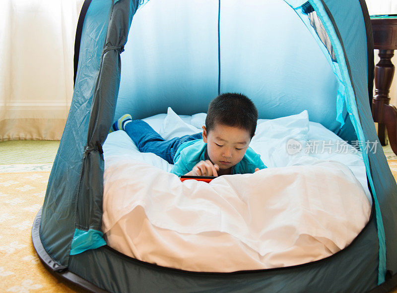 一个亚洲小男孩在帐篷里玩平板电脑