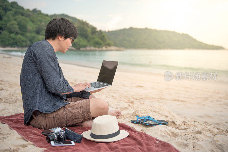 年轻的亚洲人在热带海滩上用笔记本电脑工作