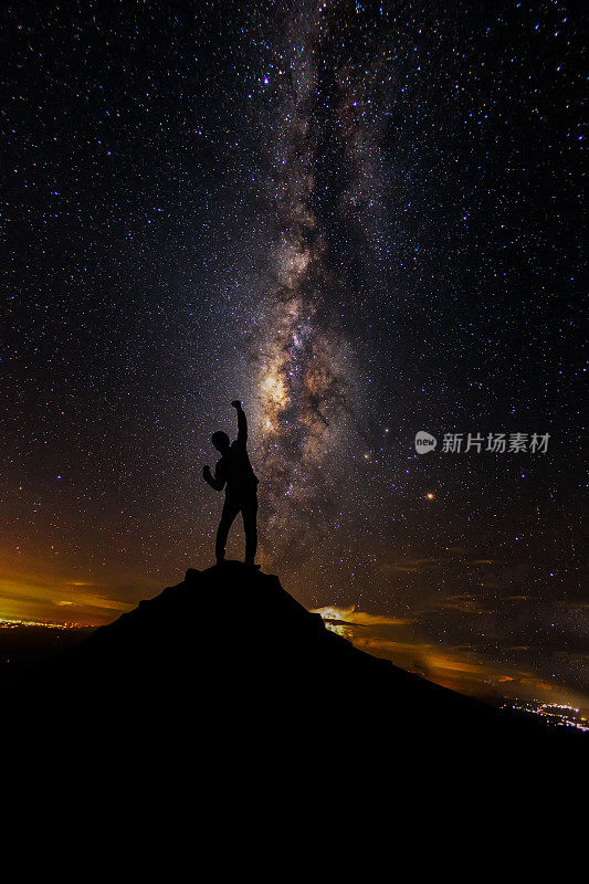 一个人的剪影站在山顶旁边的银河系，他的手在空中举起