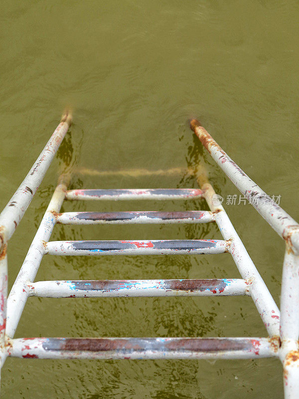 肮脏生锈的铁梯向下通向乳绿色的水
