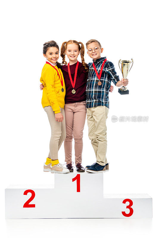 快乐的孩子与奖章和奖杯微笑，站在冠军领奖台上，看着相机孤立的白色