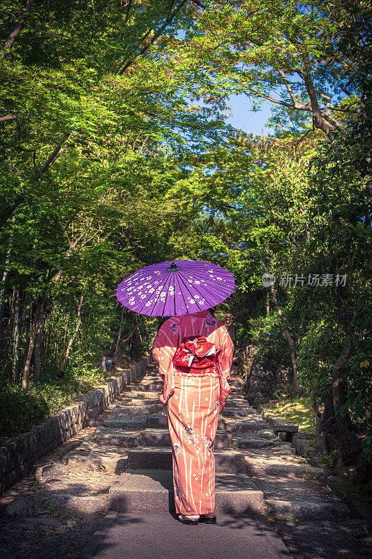 美丽的亚洲女人走过花园在她的和服在京都，日本