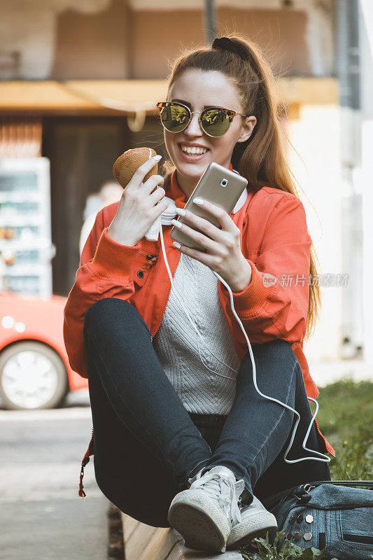 吃着冰淇淋的迷人女人正坐在户外，用智能手机输入信息