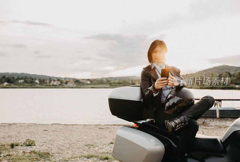 漂亮年轻性感的女人穿着皮衣坐在摩托车上的湖边。