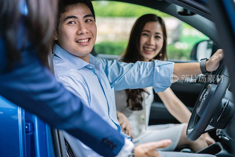 亚洲女销售员邀请和介绍夫妇客户试驾新现代汽车展示厅，汽车服务理念