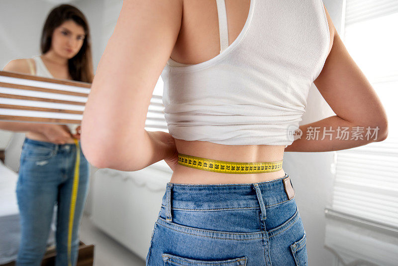 一个苗条的女人正在镜子前用卷尺量自己的腰围