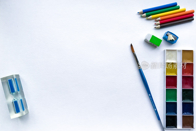 平铺的沙漏和文具学校，创意，绘画和工艺品(颜料，彩色铅笔，橡皮，卷笔刀)与白色纹理粗糙的水彩纸上的文字空间
