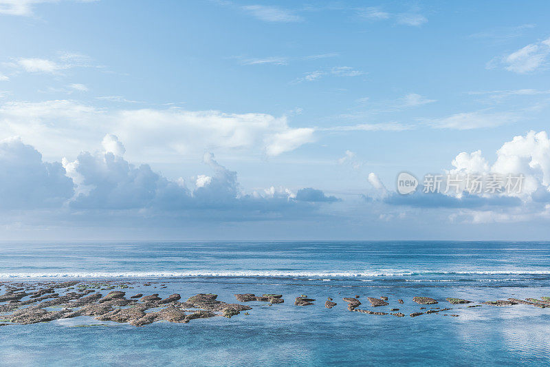 背景是巴厘岛、蓝绿色的印度洋和蓝色多云的天空