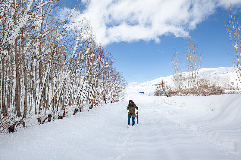 成年妇女穿着暖和的衣服在雪地上行走在农村