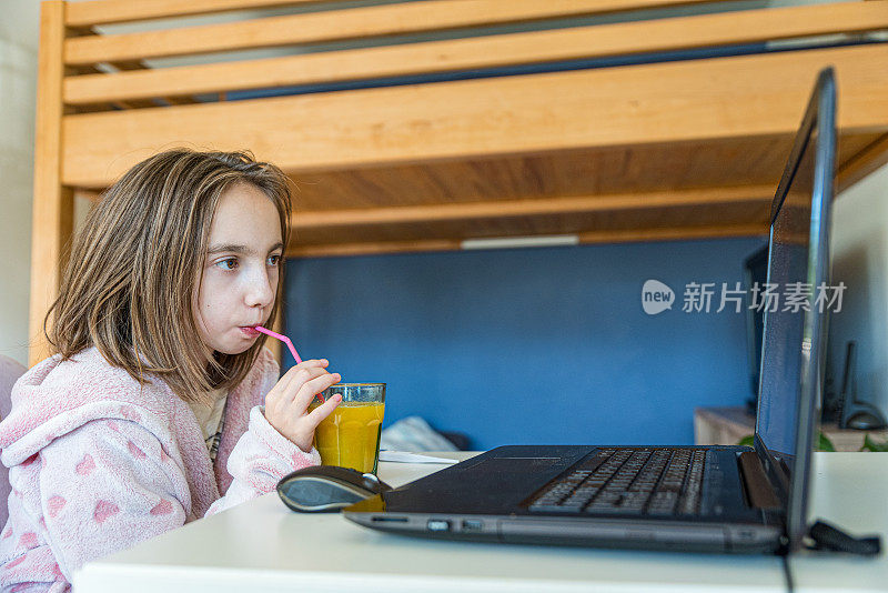 穿着睡衣的年轻女孩通过在家休息、喝橙汁和使用笔记本电脑从流感中恢复