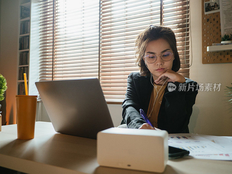 一位亚洲女性在家里开电话会议时使用笔记本电脑。