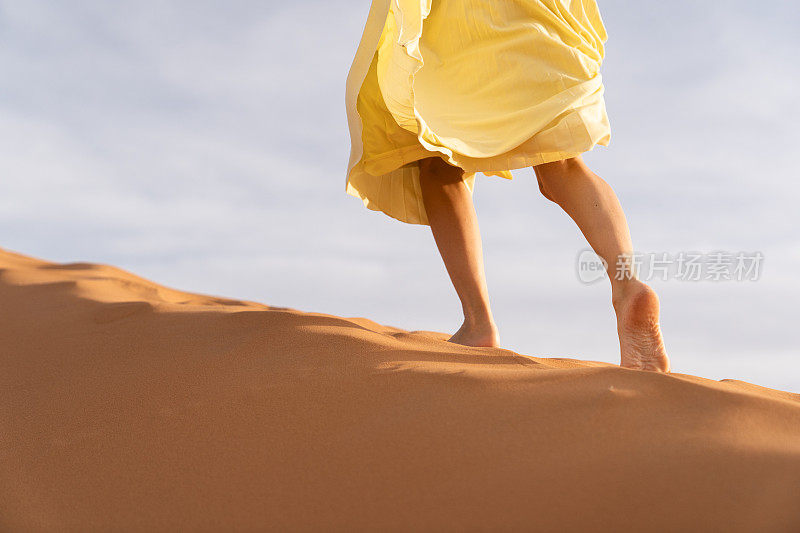 一个年轻的白种女人跑过沙丘的顶部，用她的手拿着长裙。梅尔祖加(撒哈拉)沙漠的日出。