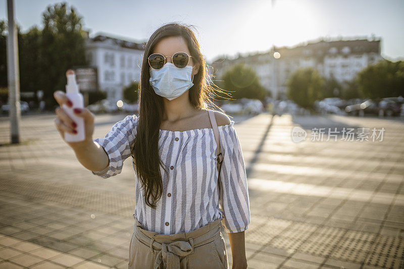 一名年轻女子戴着外科口罩，手上涂着洗手液，在封锁期间站在空荡荡的城镇广场上