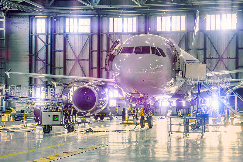 民用飞机在机场机库进行发动机维修和机身检修。门口有明亮的浅紫色。